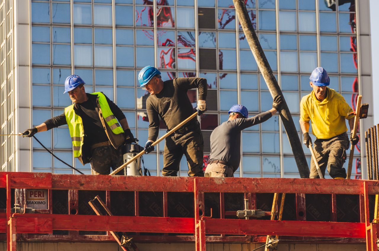 Services A group of construction workers in safety gear actively working on a high-rise building site.